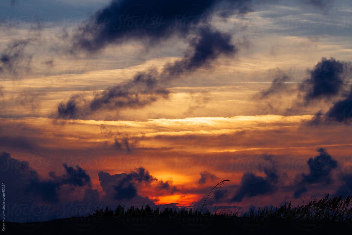 Colorful sunset and clouds over grassy dune