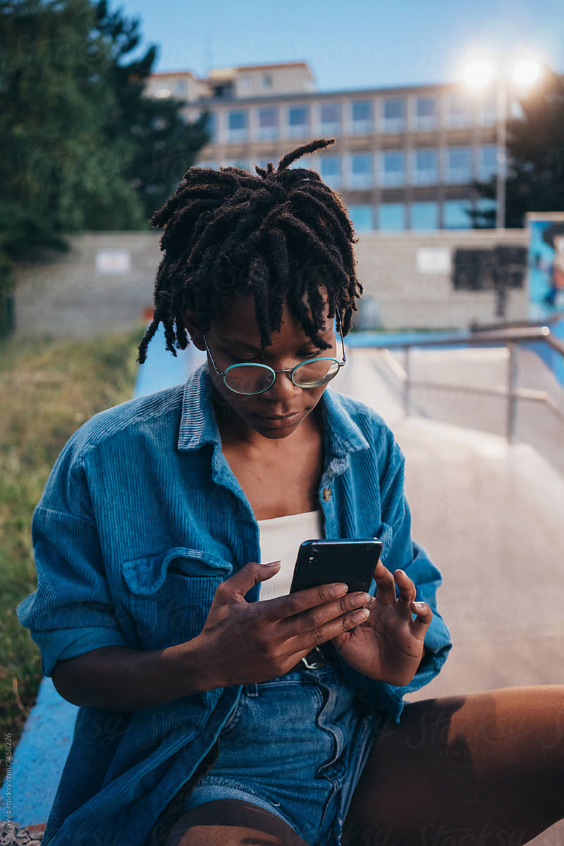 African American woman sitting in a skate park, browsing on her mobile phone