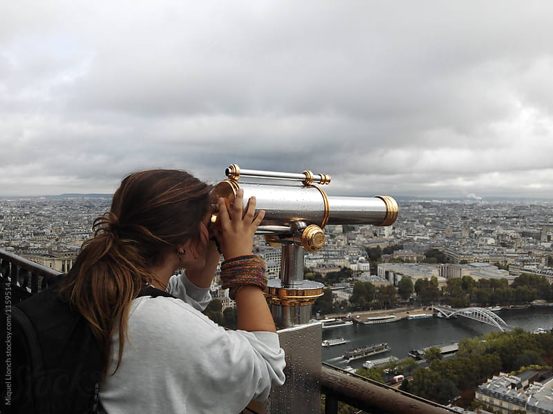 Young woman at the top of the Eiffel Tower enjoying the view with a telescope