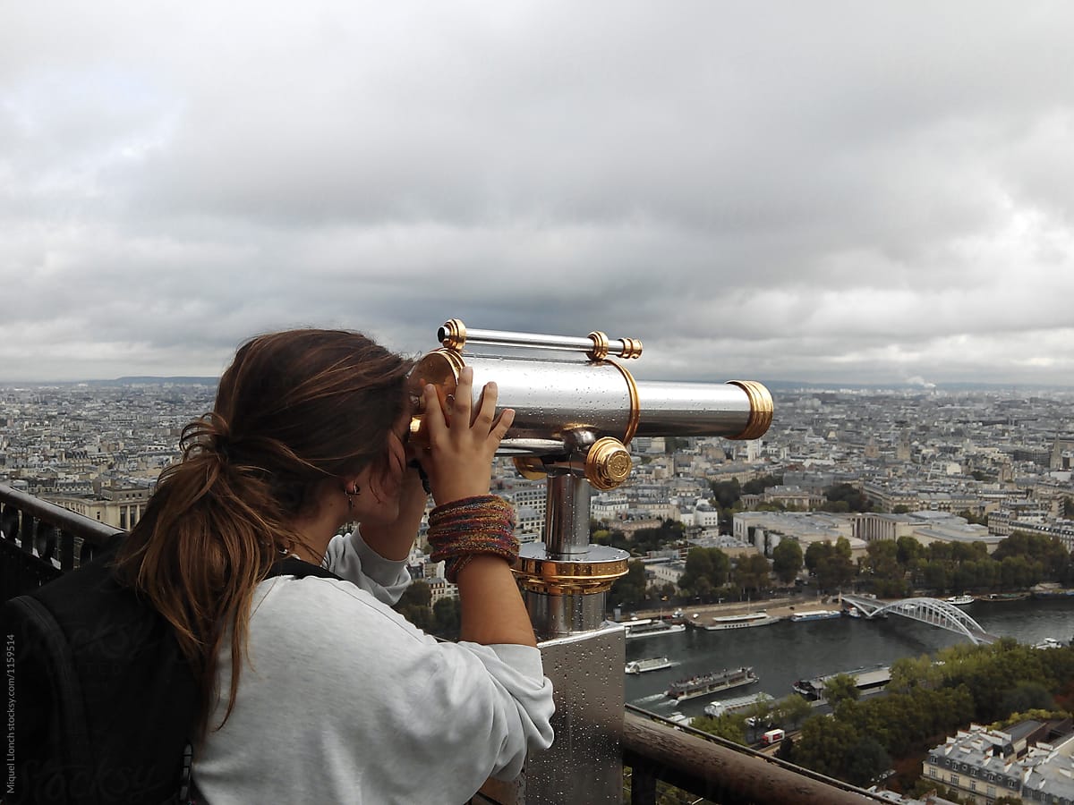 Young woman at the top of the Eiffel Tower enjoying the view with a telescope