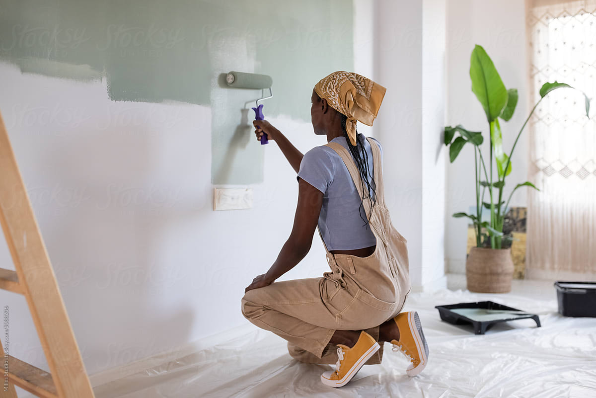 African American woman painting wall over sockets