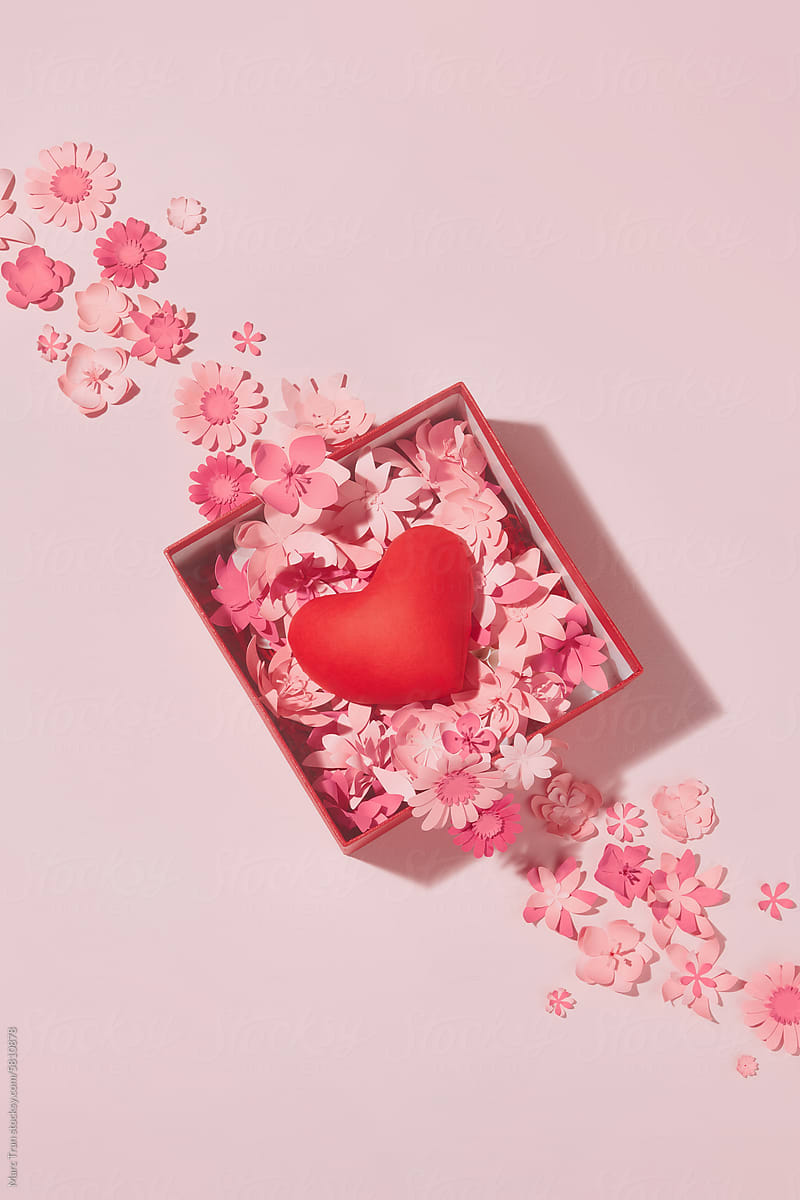 A gift box with a heart inside and paper flowers on pink background
