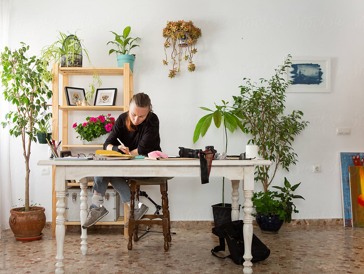 Woman works at a desk in a house plant filled home office