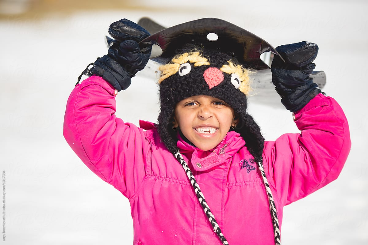 A smiling girl holding her plastic sled over her head