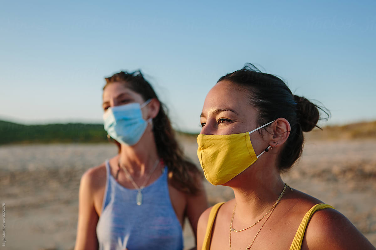 Two women in facemasks on the beach