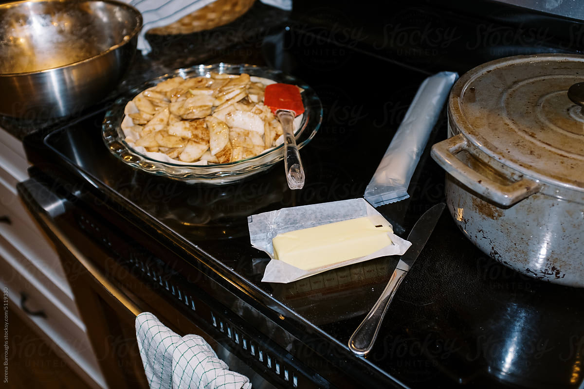 messy stovetop with cookware and an apple pie on top