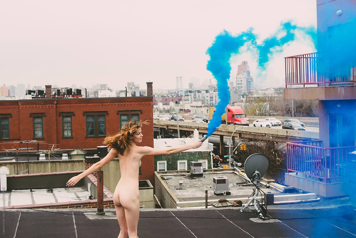 Young woman on rooftop, naked, playing with smoke bomb
