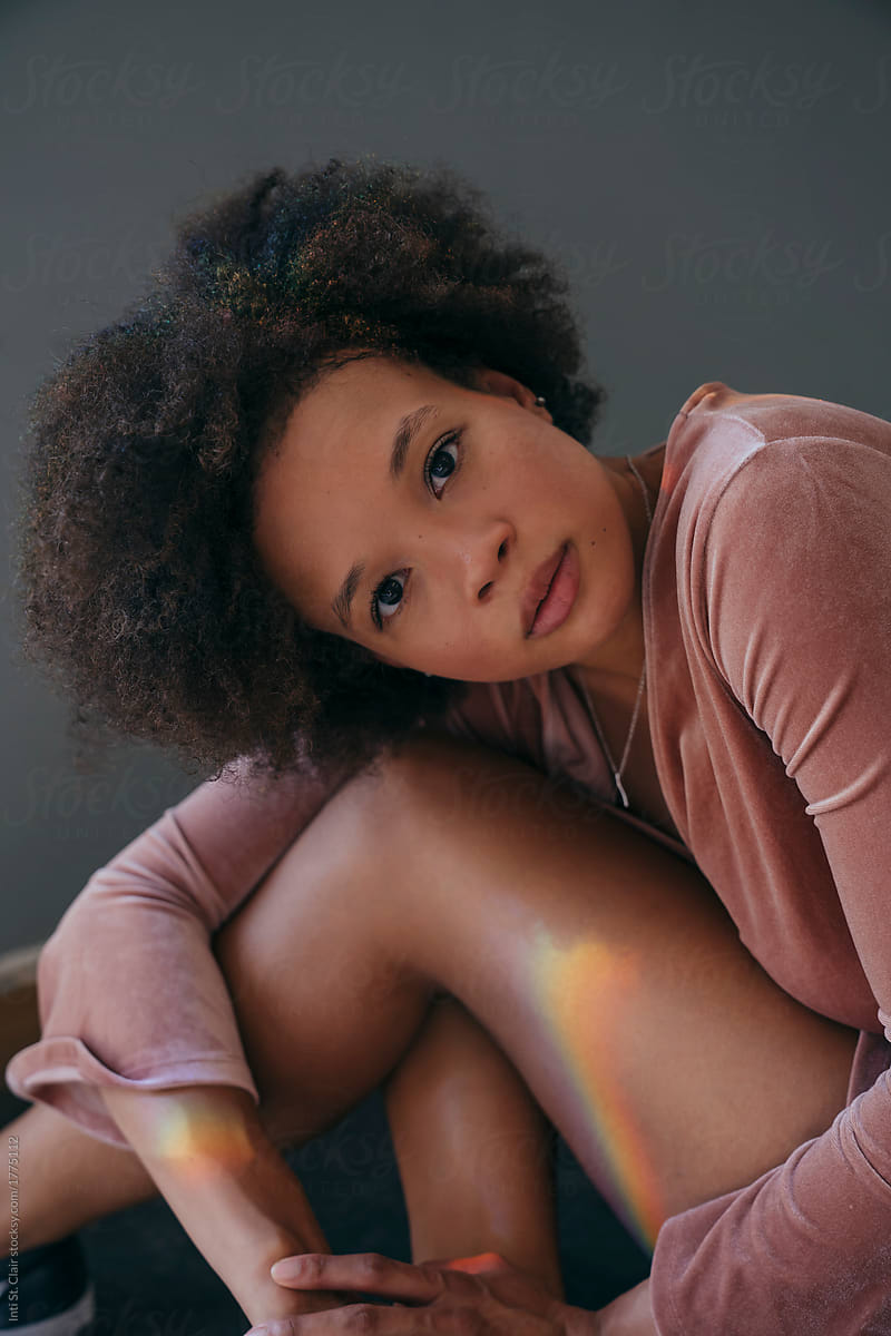 Woman with afro sitting hugging knees and looking at camera