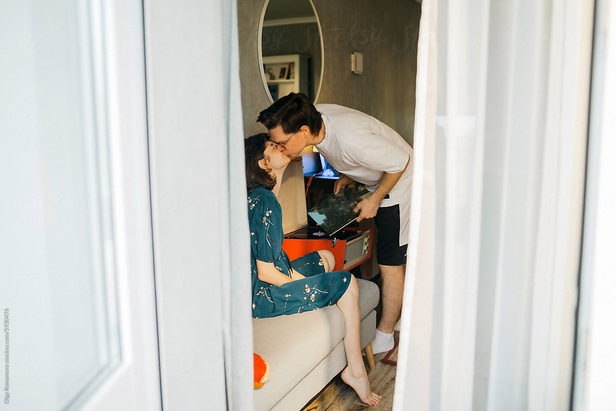 Kiss of a happy couple at home in their living room through the window