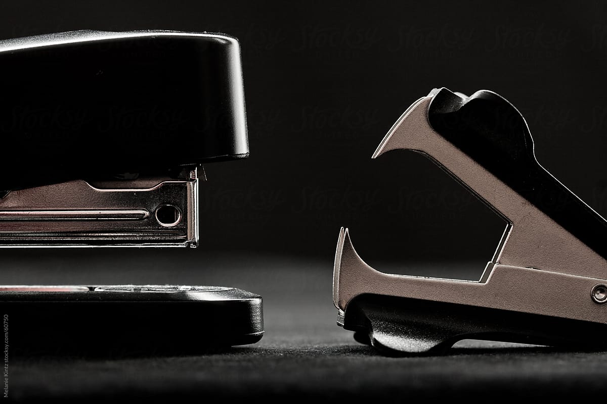 Stapler and staple remover  opposite to one another before black background