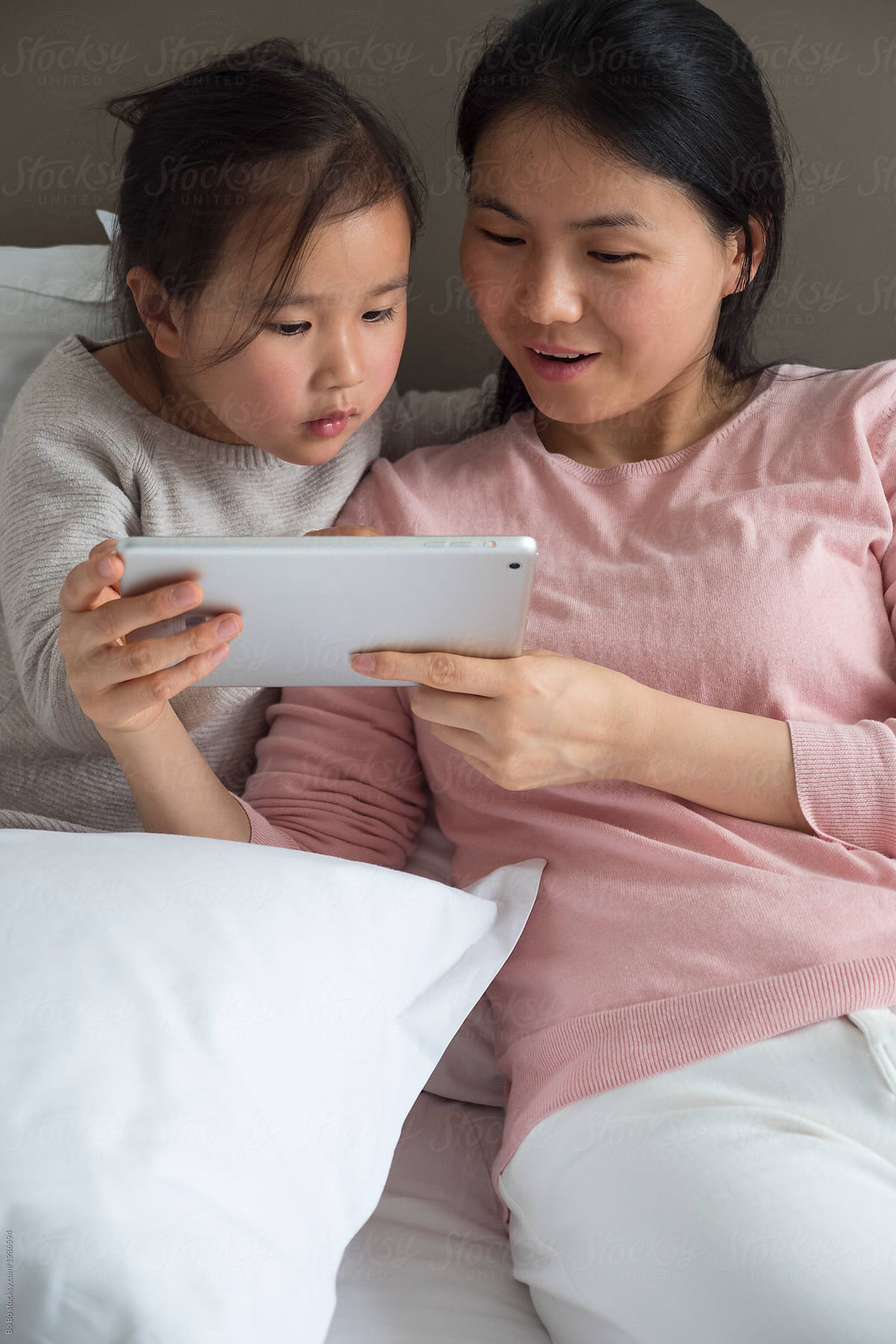 Little asian girl with her mother in bed using tablet