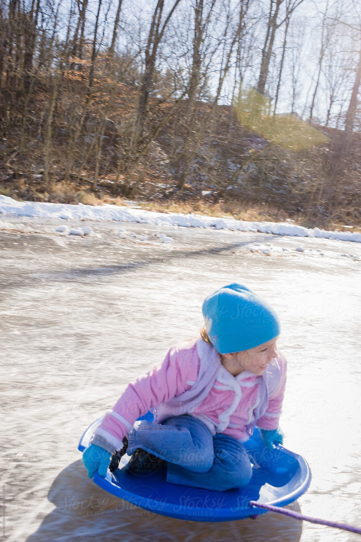 Happy Little Girl Sledding on Frozen Pond