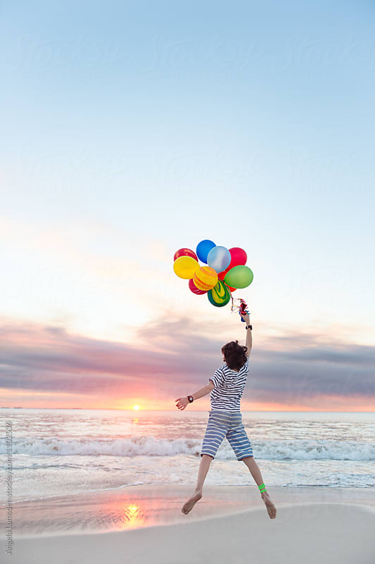 Child jumping with balloons at sunset