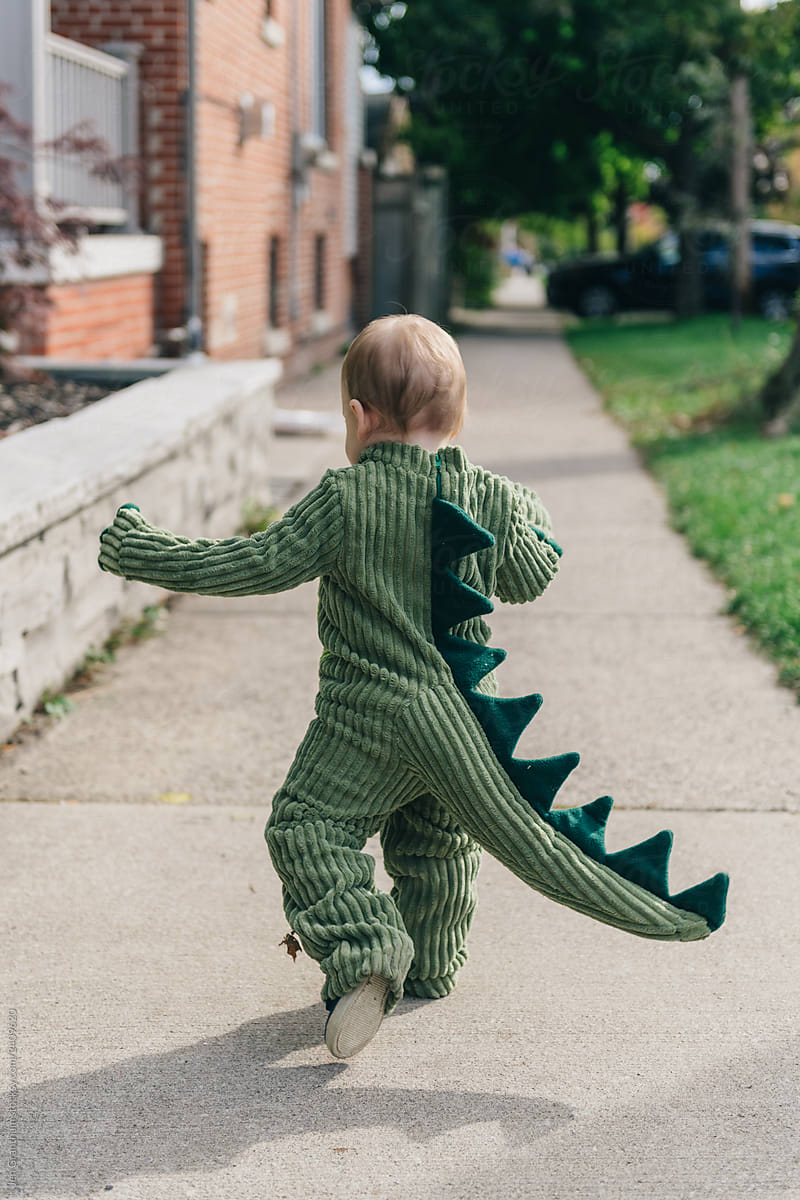 Toddler running down the sidewalk in a dinosaur costume