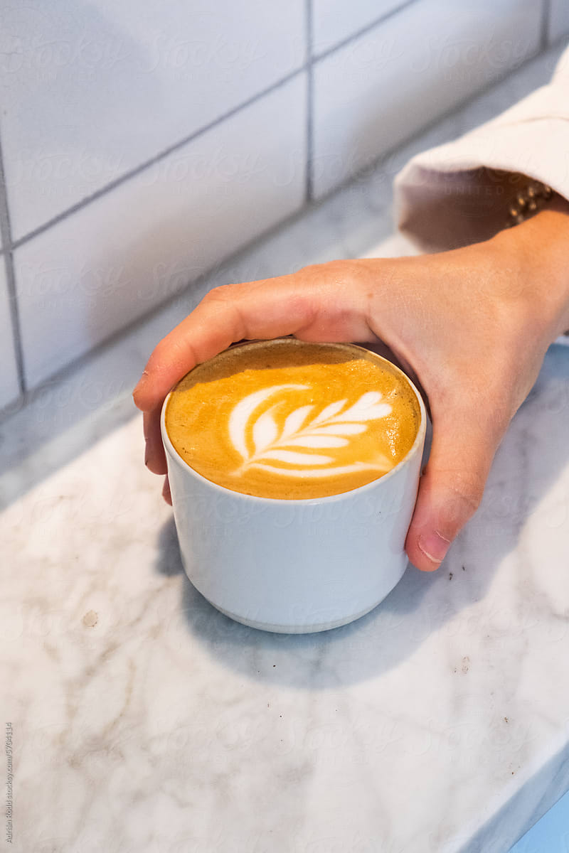 Close up of a hand holding a coffee cup with latte art decorations