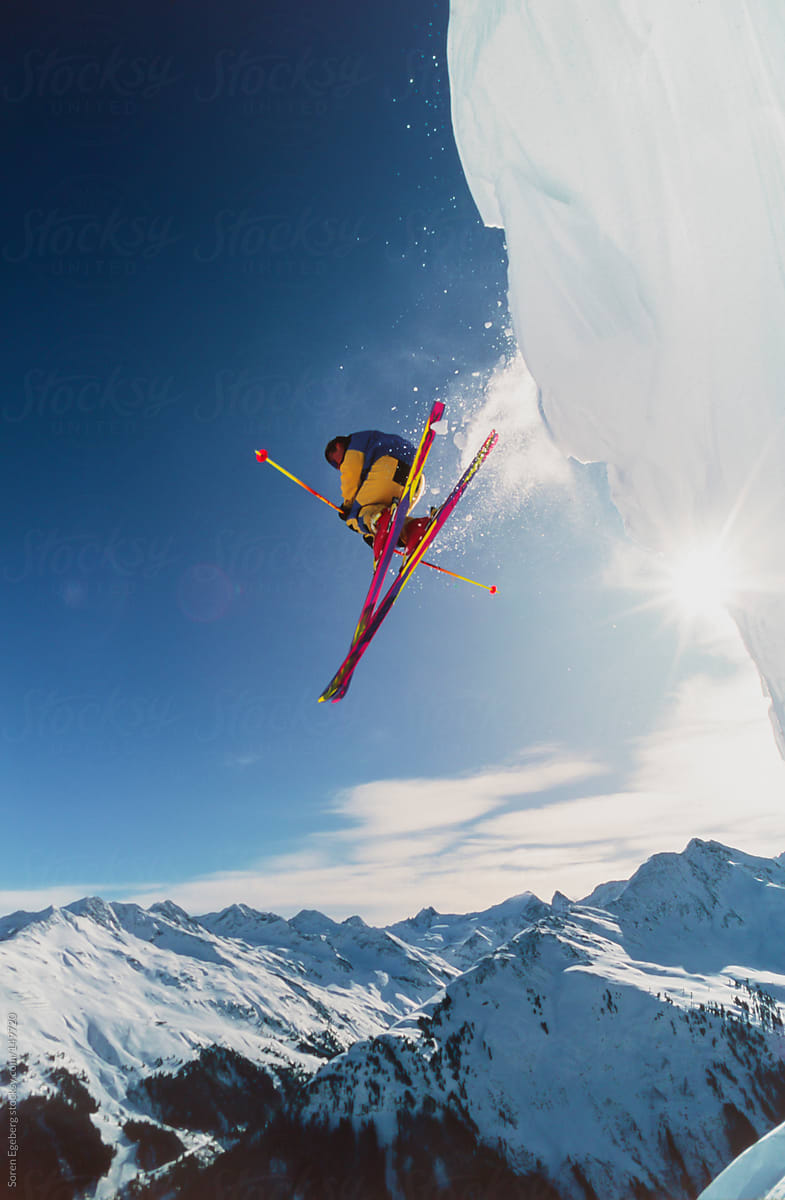 Skier jumping off snow cornice in winter mountain landscape