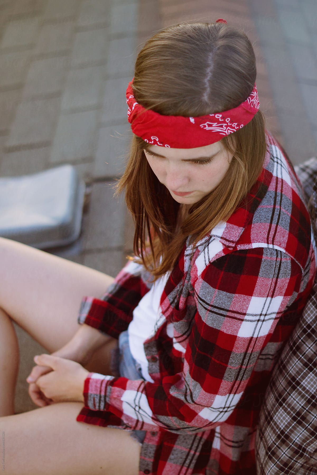Teenage girl wearing red flannel and bandanna sits on roof top