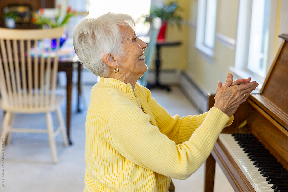 Happy Senior Citizen woman at Home playing piano and clapping