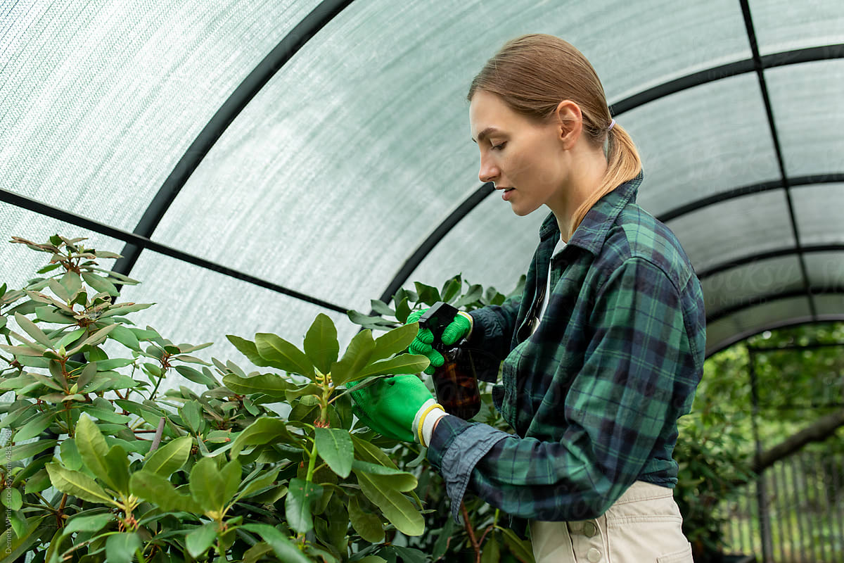 White blonde woman works with plants inside greenhouse