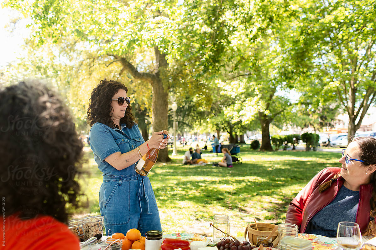 Woman opening bottle of wine during picnic with friends