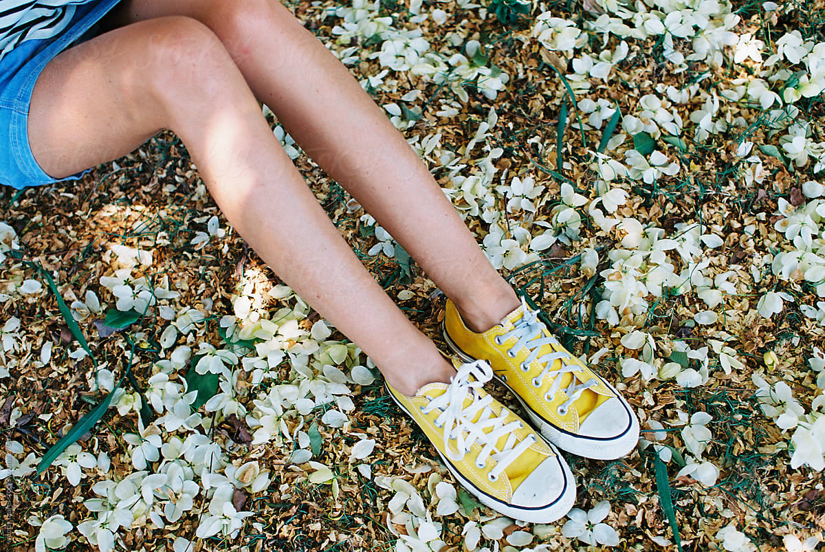 blonde woman laying in grass with flowers in striped tee and underwear and jean skirt and yellow tennis shoes