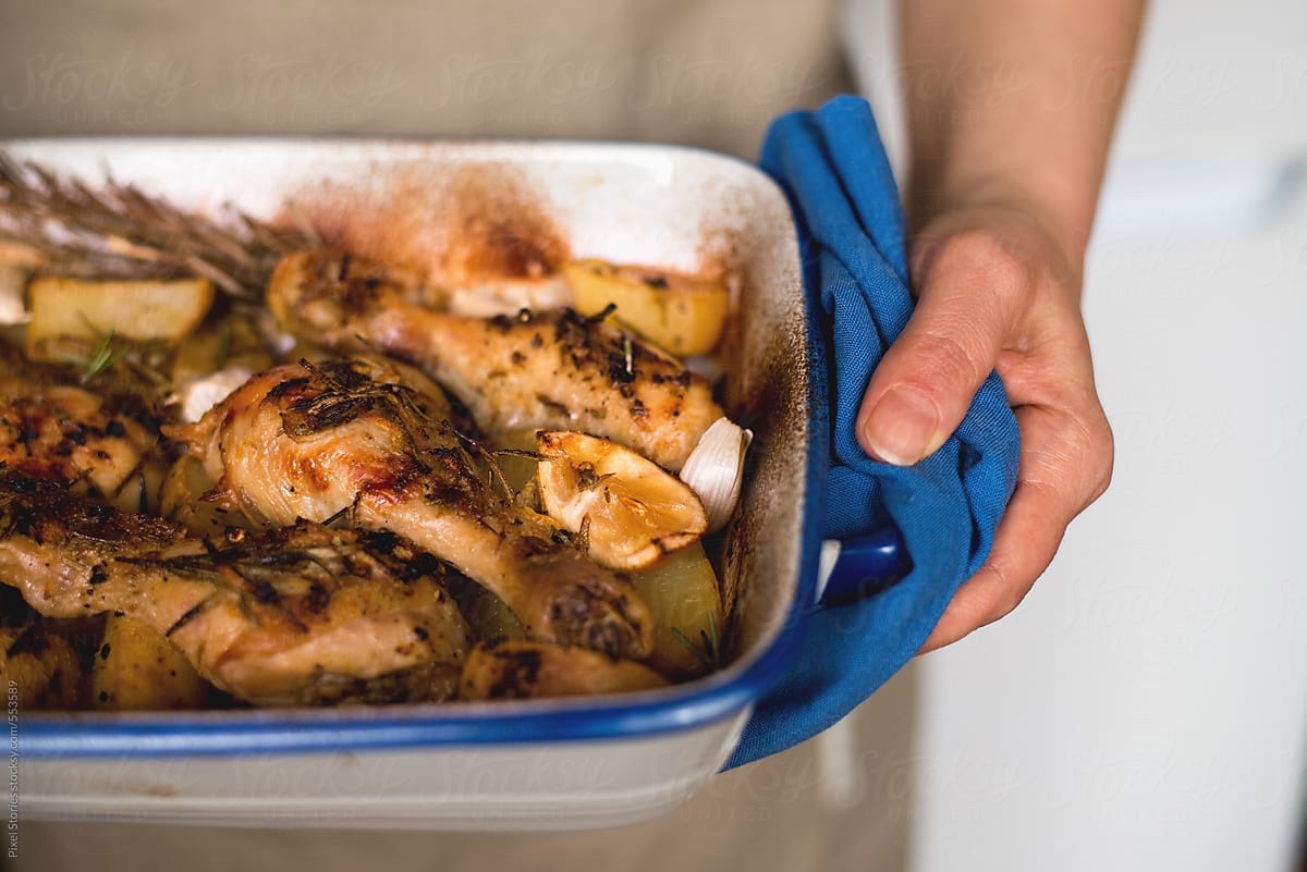 Woman holding baking tray of chicken legs with potatoes