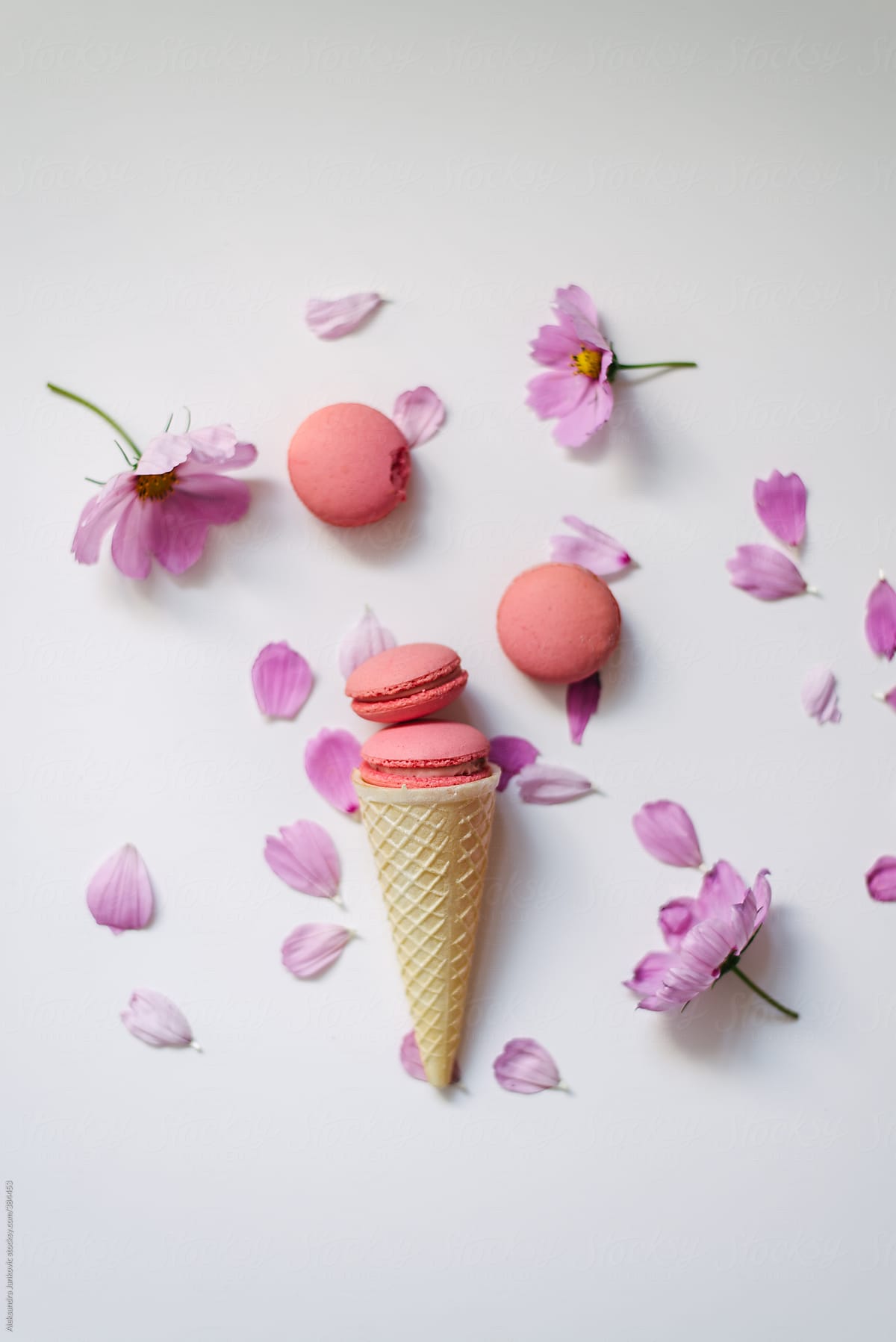 Pink macaroons in cone and flowers on white background
