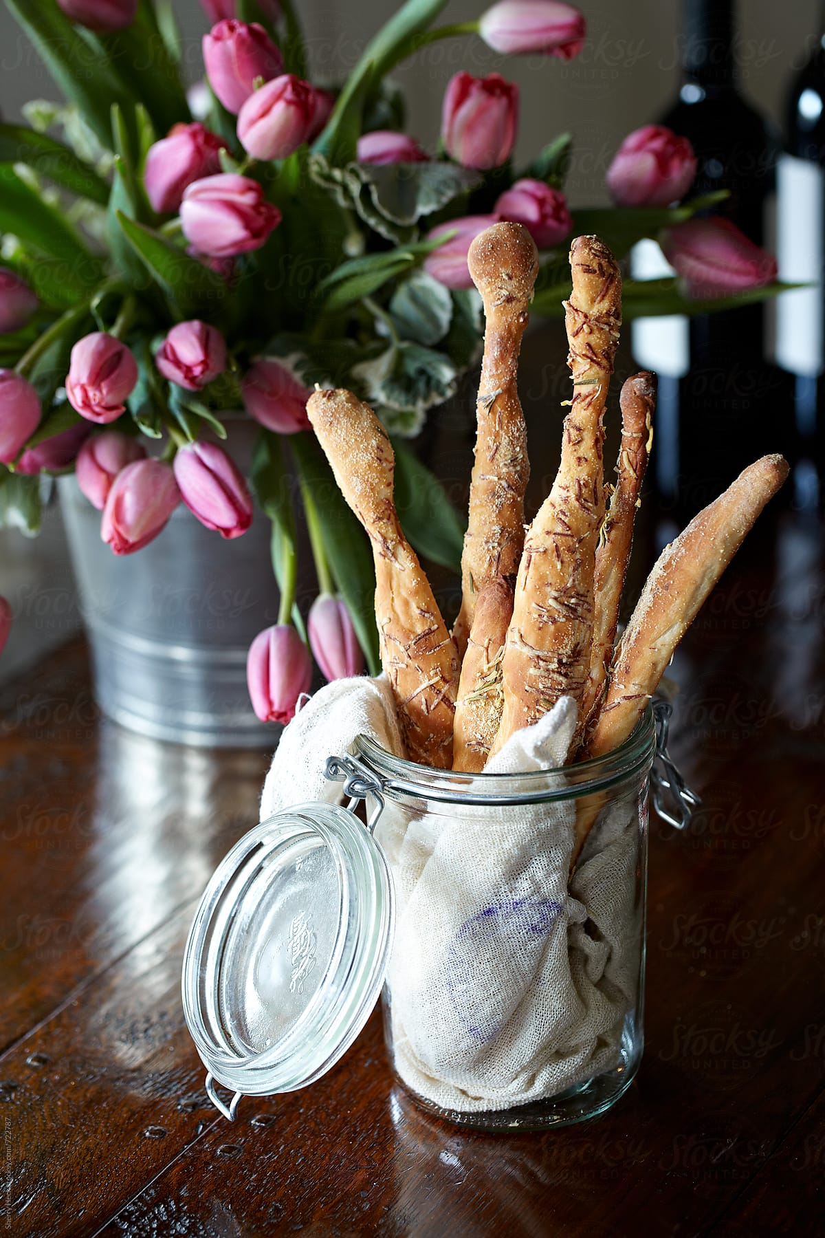 Handmade breadsticks in a jar on a dark table with tulips and wine
