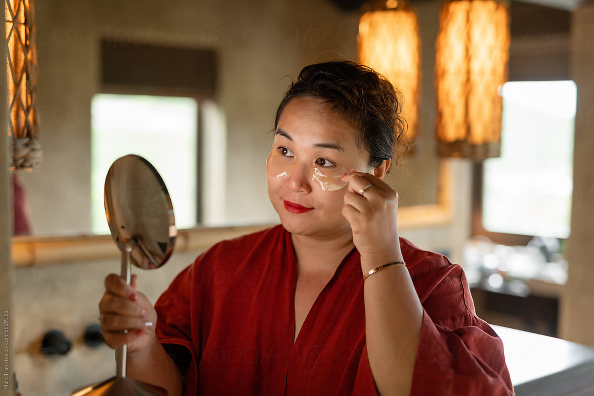 Satisfied woman in red bathrobe applying gold eye patches
