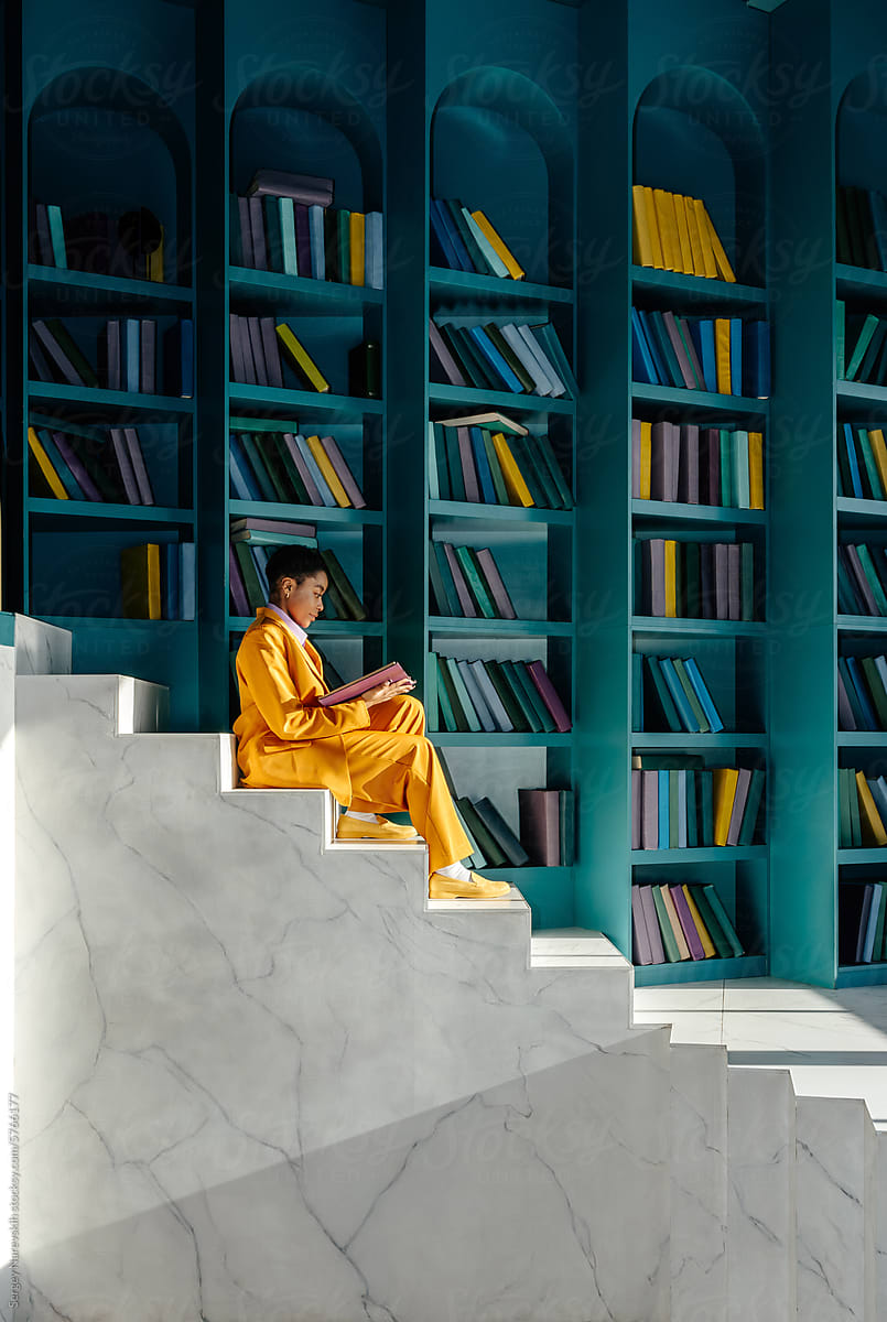 Female in yellow suit sitting on stairs and reading book in library