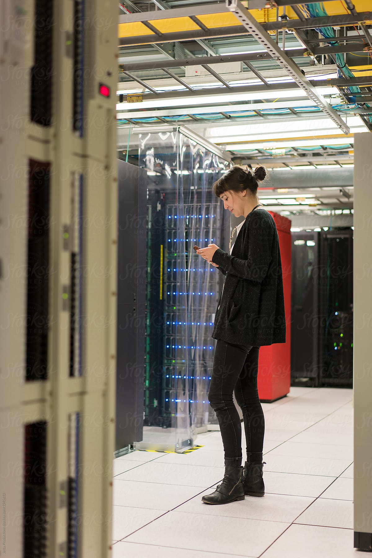 Technician stands in a server room while reading her cellphone