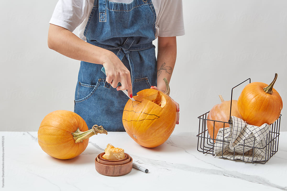 Woman carving jack-o-lanterns on marble table.