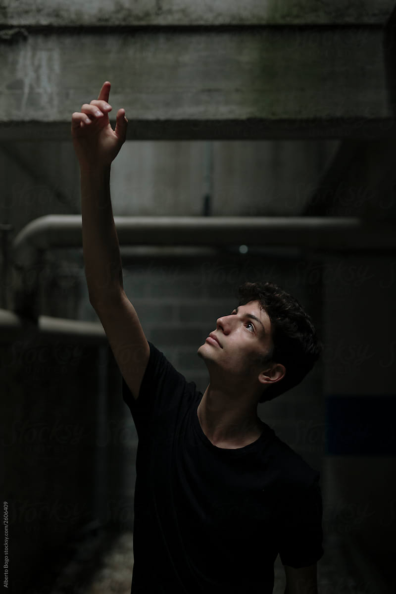 Young man raising hand on dark background