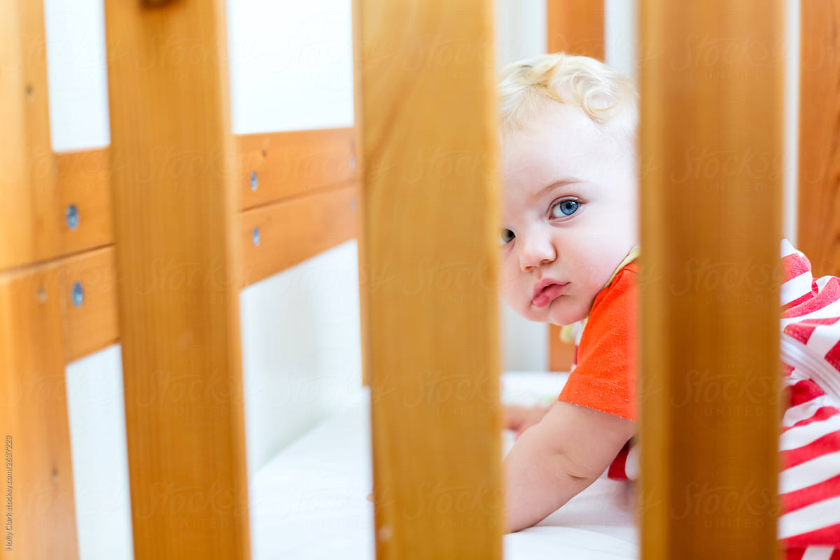 Blond child in crib peaks out between slats of crib