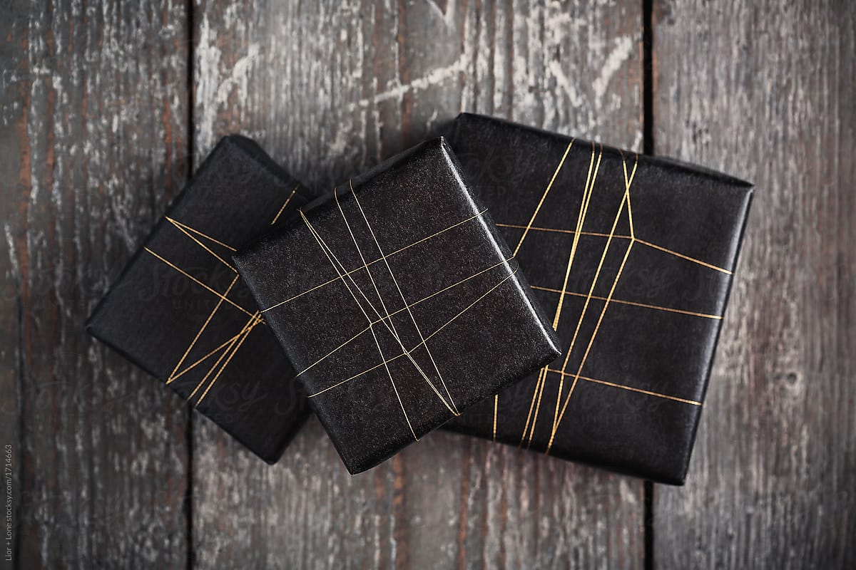 Three gifts wrapped in black with golden string on wooden surfac