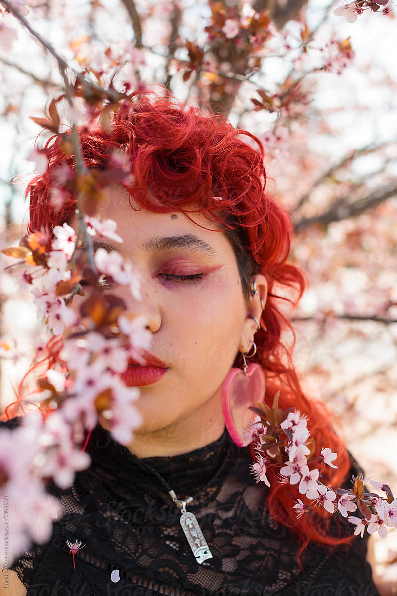Queer person posing behind almond tree in blossom with eyes closed