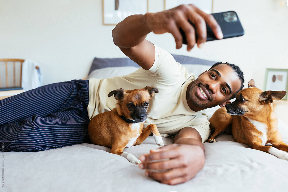 Happy owner taking selfie with dogs on bed