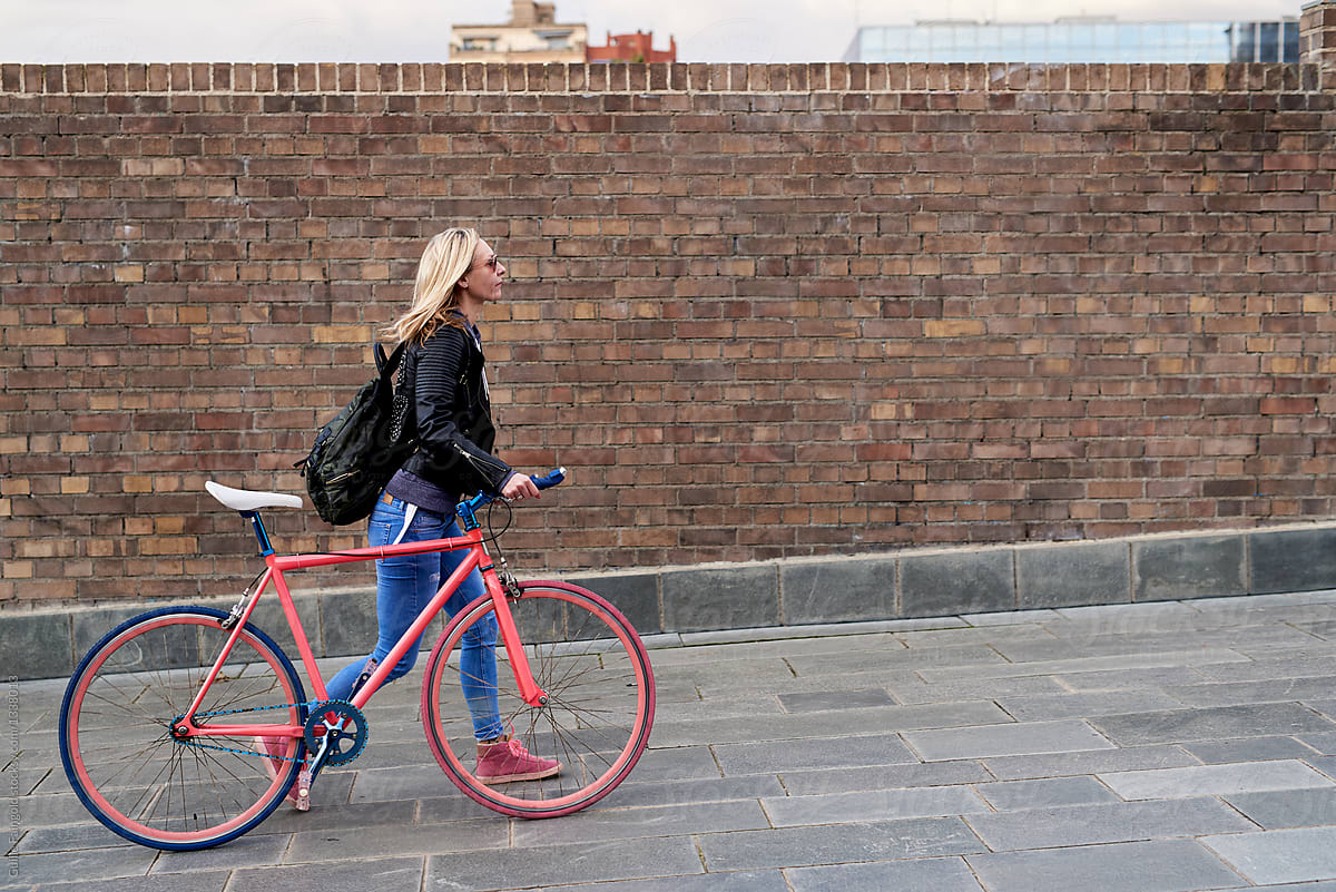 Woman with bike walking along brick wall