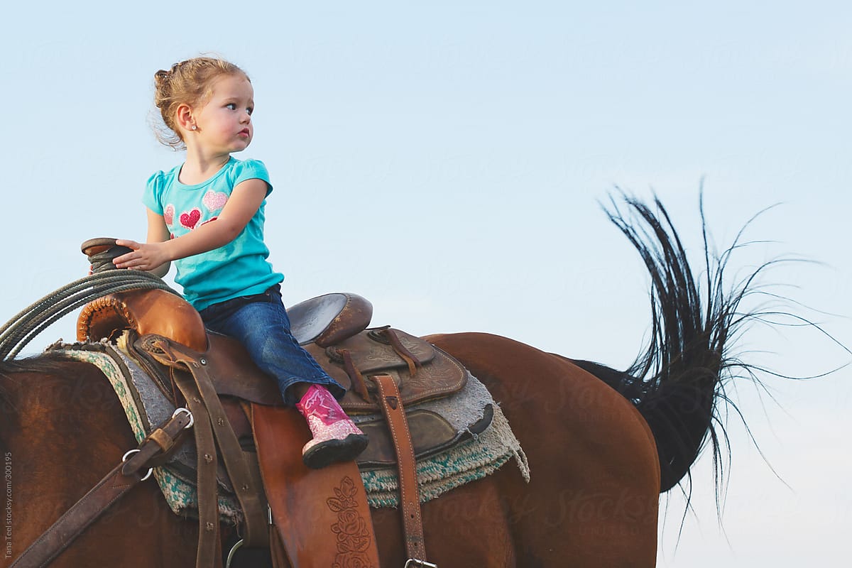 Girl sits in saddle atop a horse while he flicks his tail