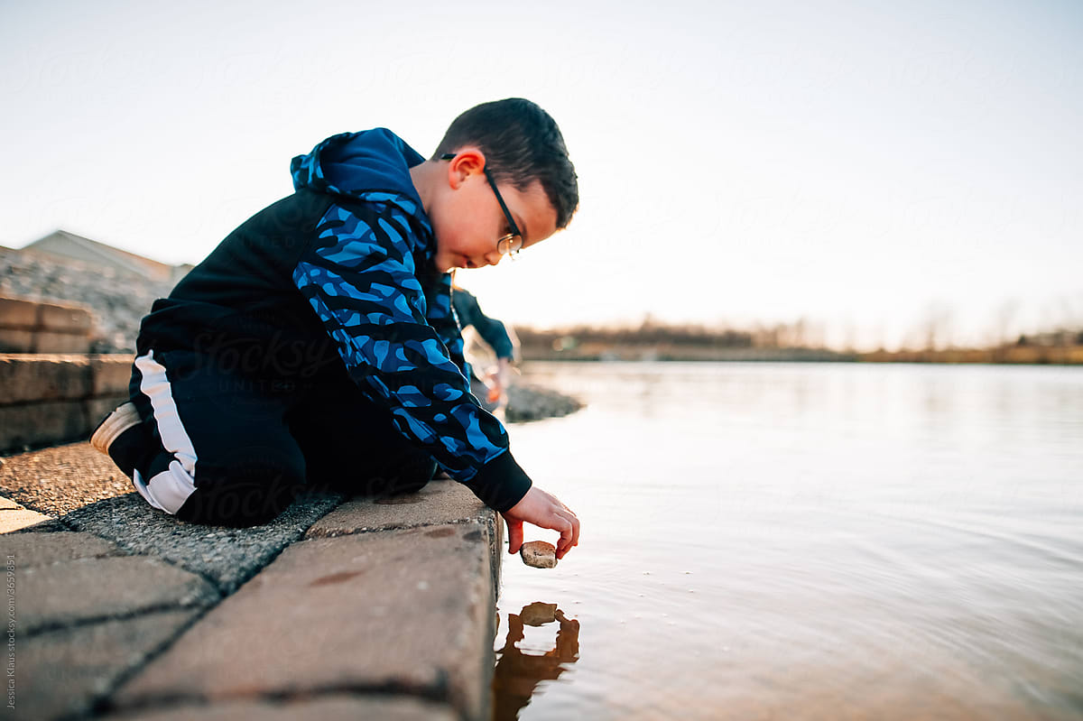 Boy holding a stone over water.