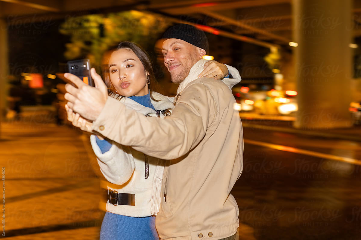 a couple smiles and takes photos with their mobile phone