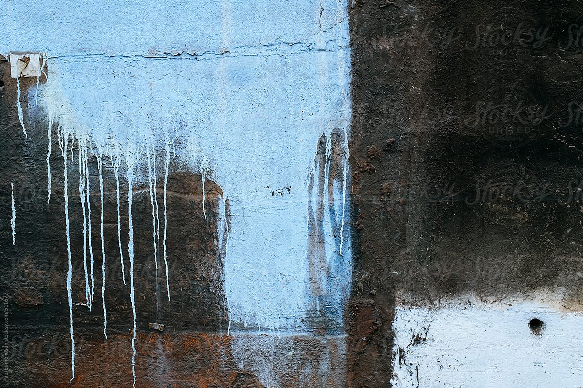 Blue paint dripping down wall of old and weathered building exterior
