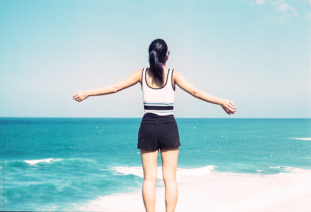 Girl Standing In Front Of A Beautiful Blue Open Ocean With Arms Spread