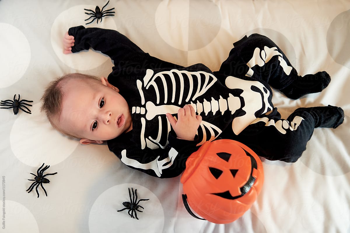 Adorable baby with trick or treat bucket on bed