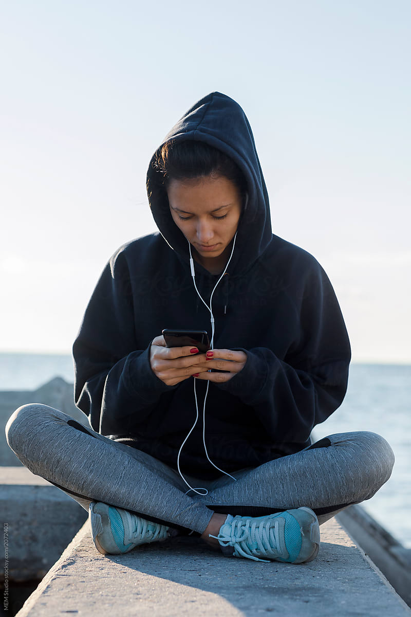 Young sporty woman listening music on her phone while having a rest from a jog
