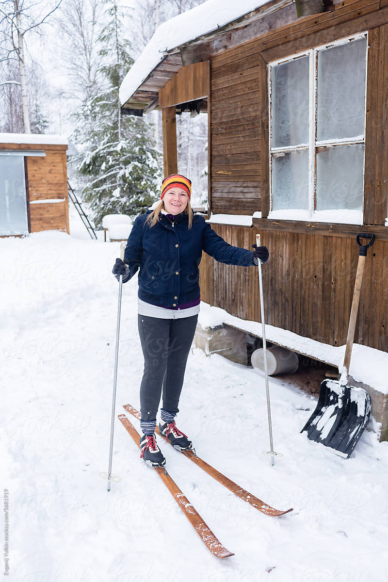 Smiling woman on skis at the wooden house