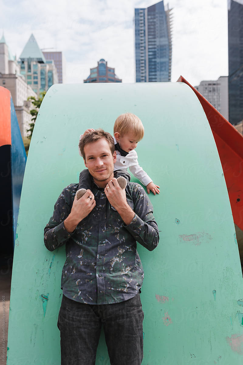 Young, cool dad holding son on his shoulders near aqua green wall in the city