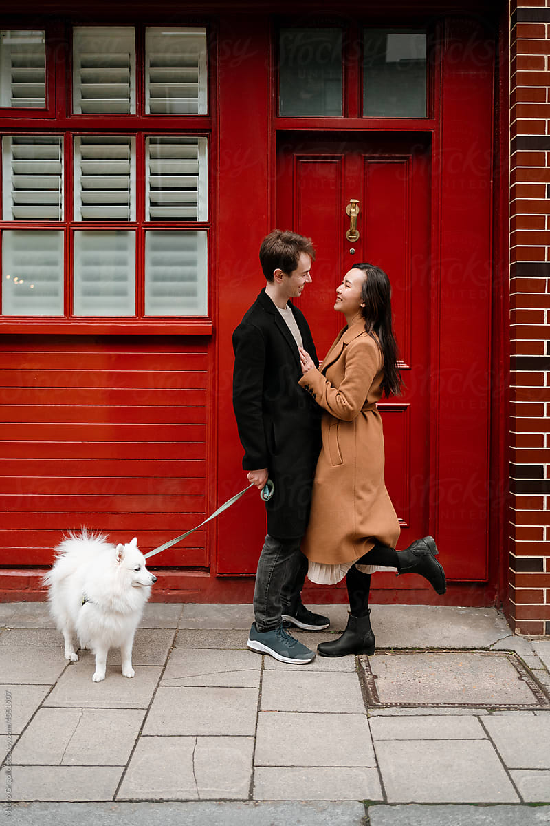 Happy lovers with their dog flirting out of a red house
