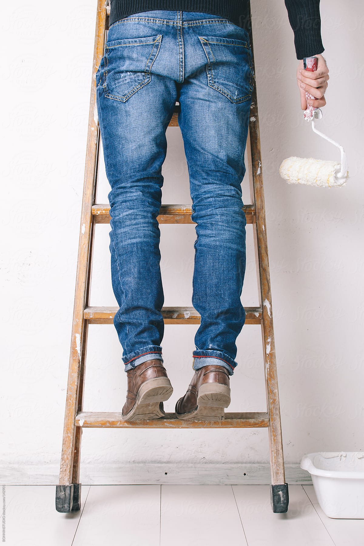 Man painting a wall on a wood ladder.