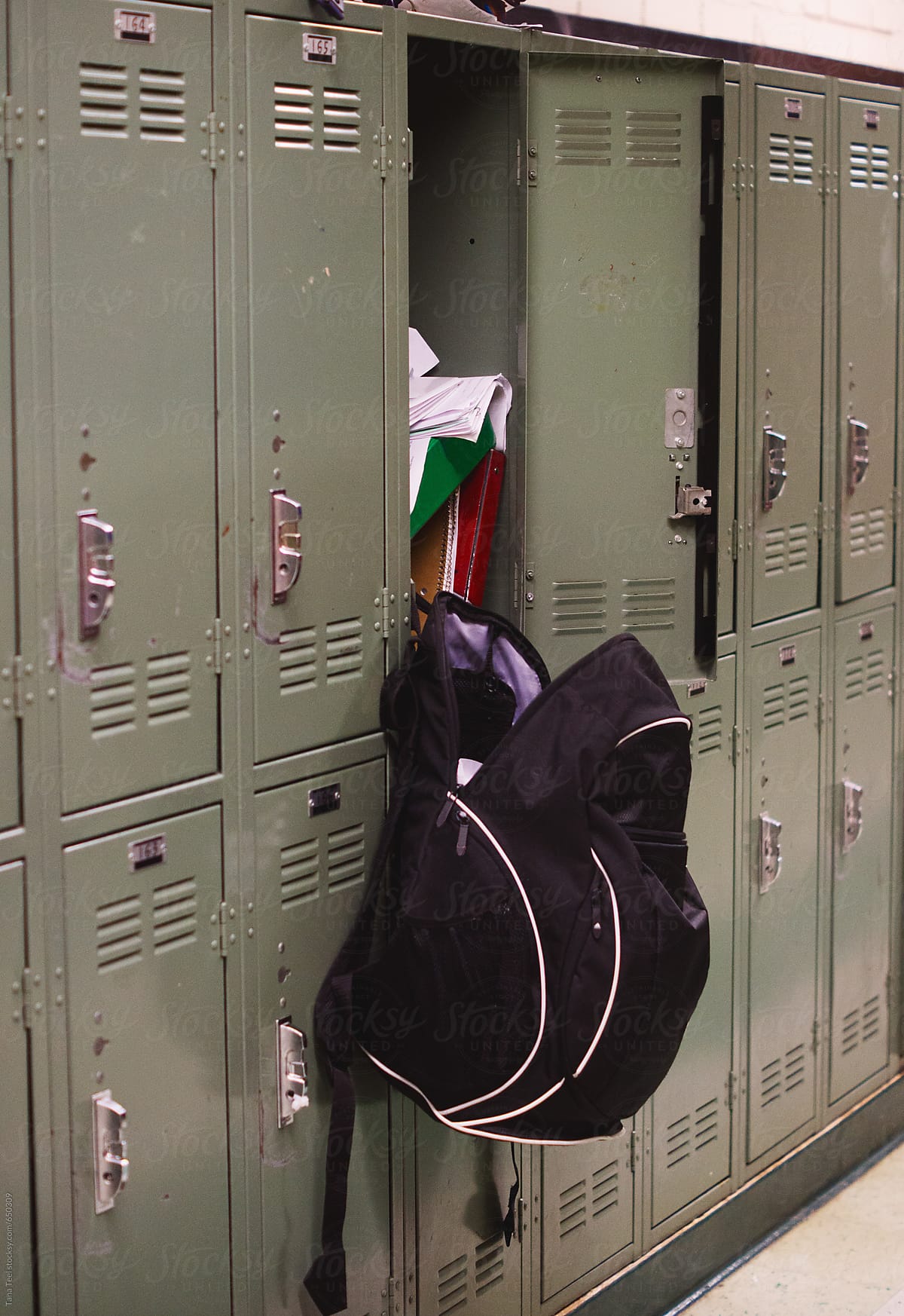 Backpack hangs from open messy locker in school hallway